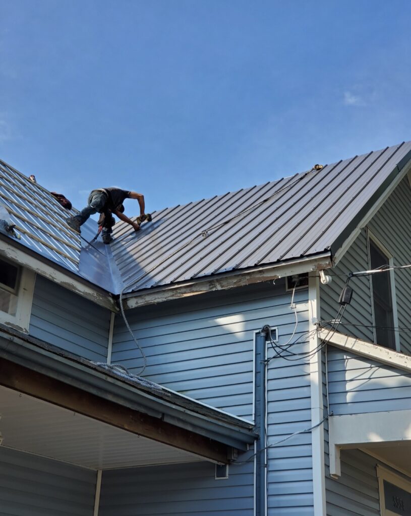 Roofer stand between two roofs installing a metal roof